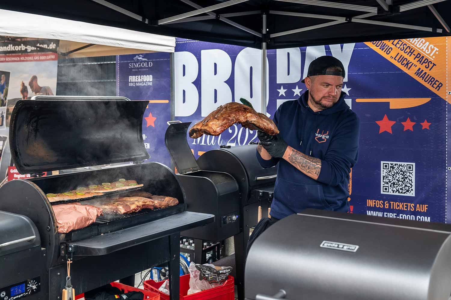 Man grilling meat at a BBQ event under a tent.