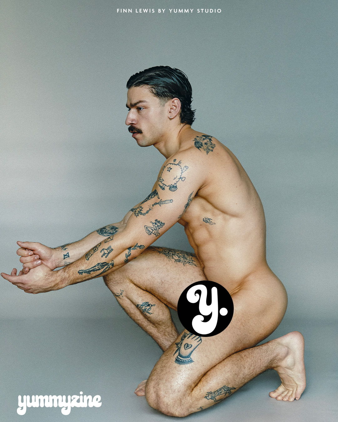 Man with tattoos posed kneeling, covering private areas with a logo.