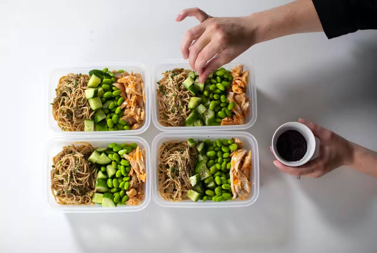 Top-down view of someone putting the sesame noodle ingredients into individual containers for meal planning.