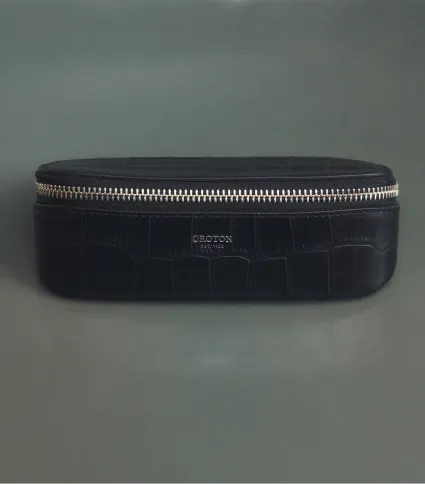 Black zippered case with a crocodile texture on a gray background.