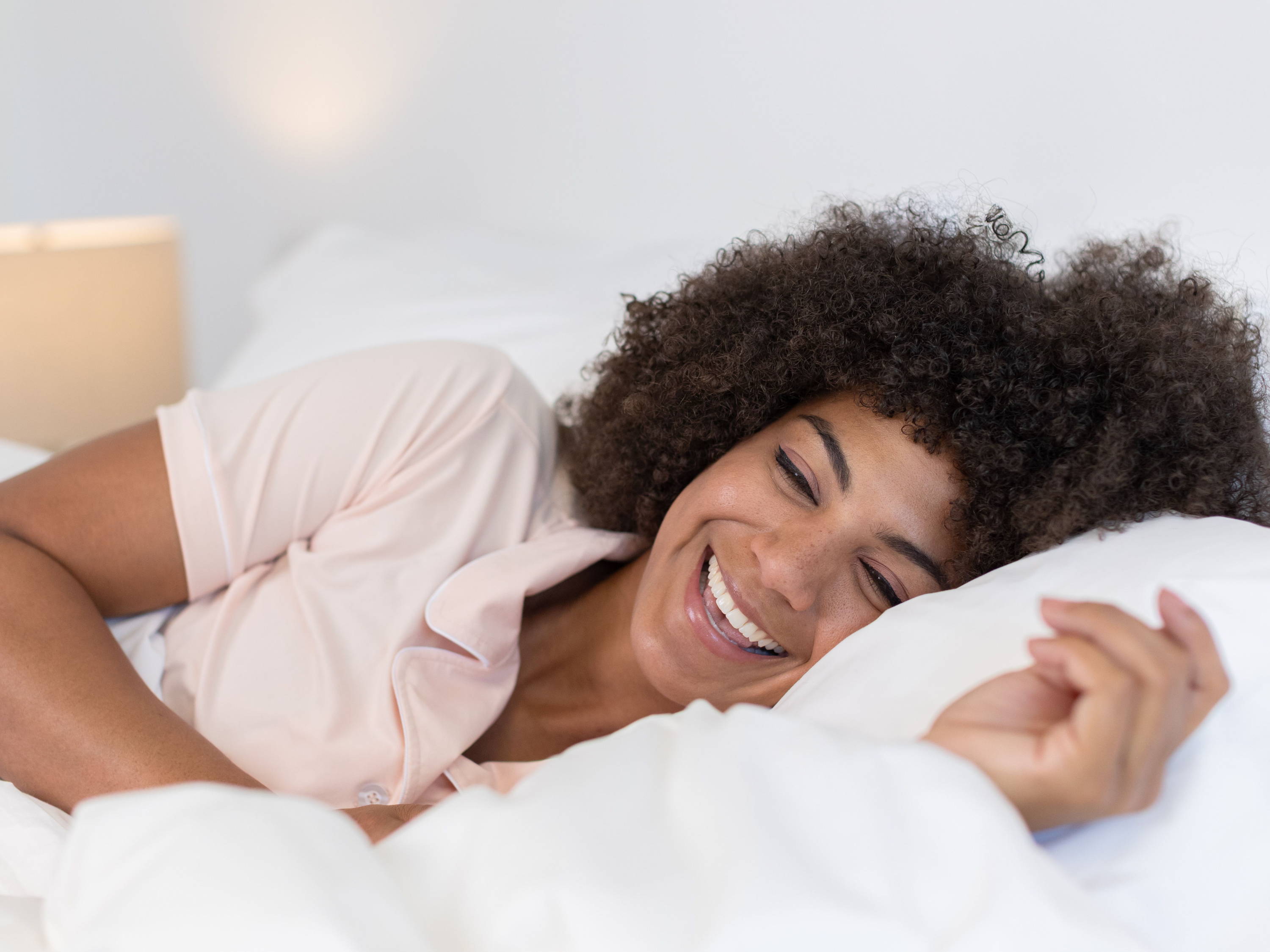 Smiling woman in bed, pink pjs, and white comfortcore and percale QuickZip bedding