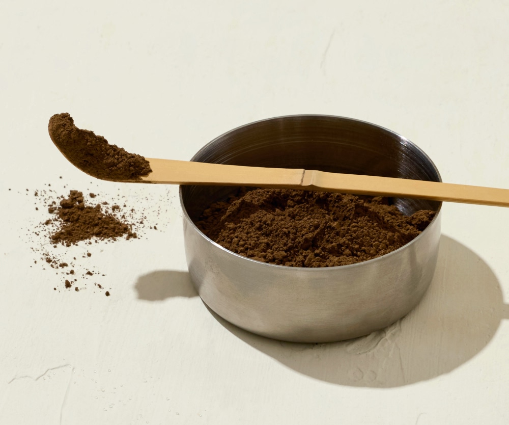 A wooden spoon with coffee grounds in a metal bowl.