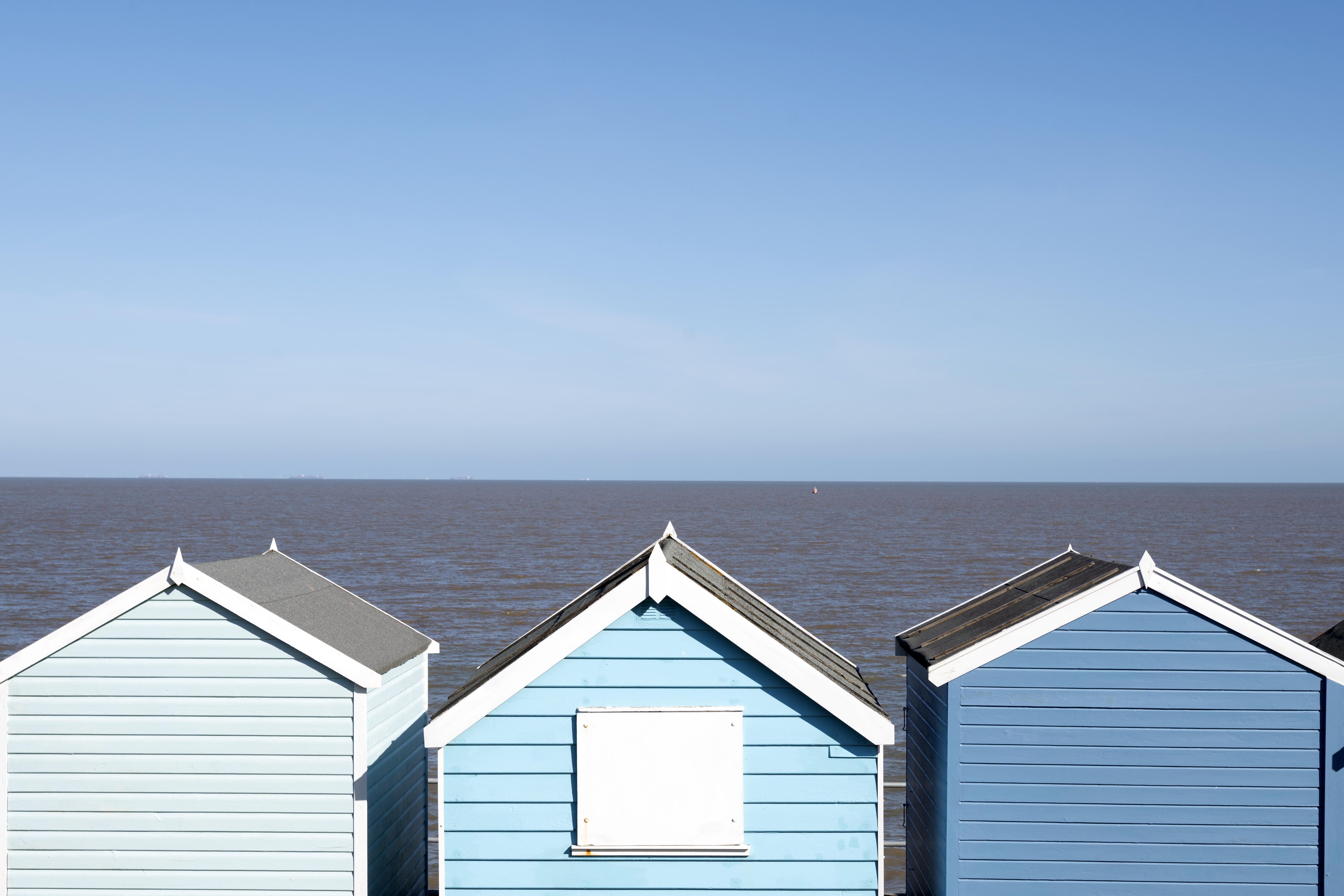 Row of blue beach huts against a clear sky and ocean.
