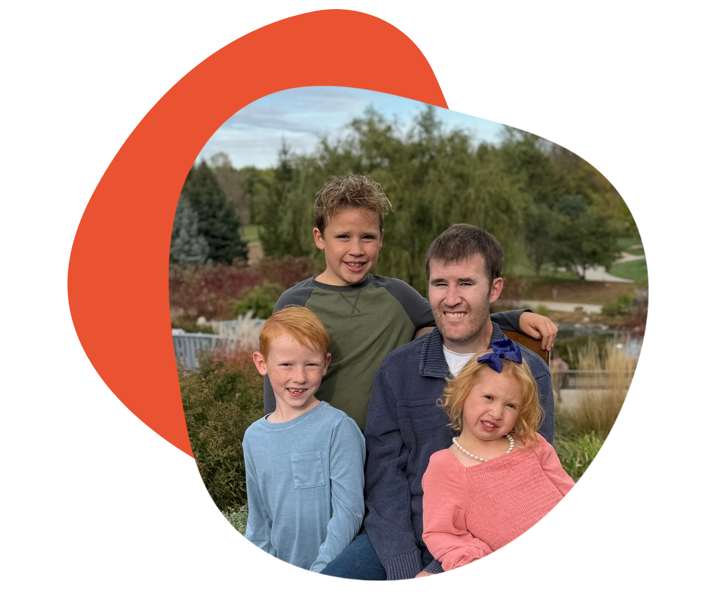 A man and three children posed outdoors near a pond.