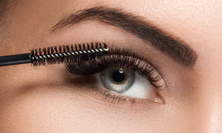 Close-up of a woman applying mascara to her eyelashes.