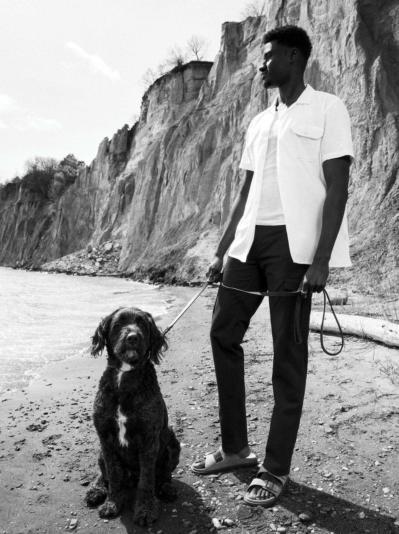 Tall man wearing a white button shirt and blue cargo pants while holding a dog on a leaseh
