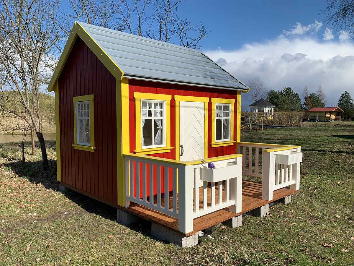 Custom playhouse in red and yellow color with a gery roof in the countryside by WholeWoodPlayhouses