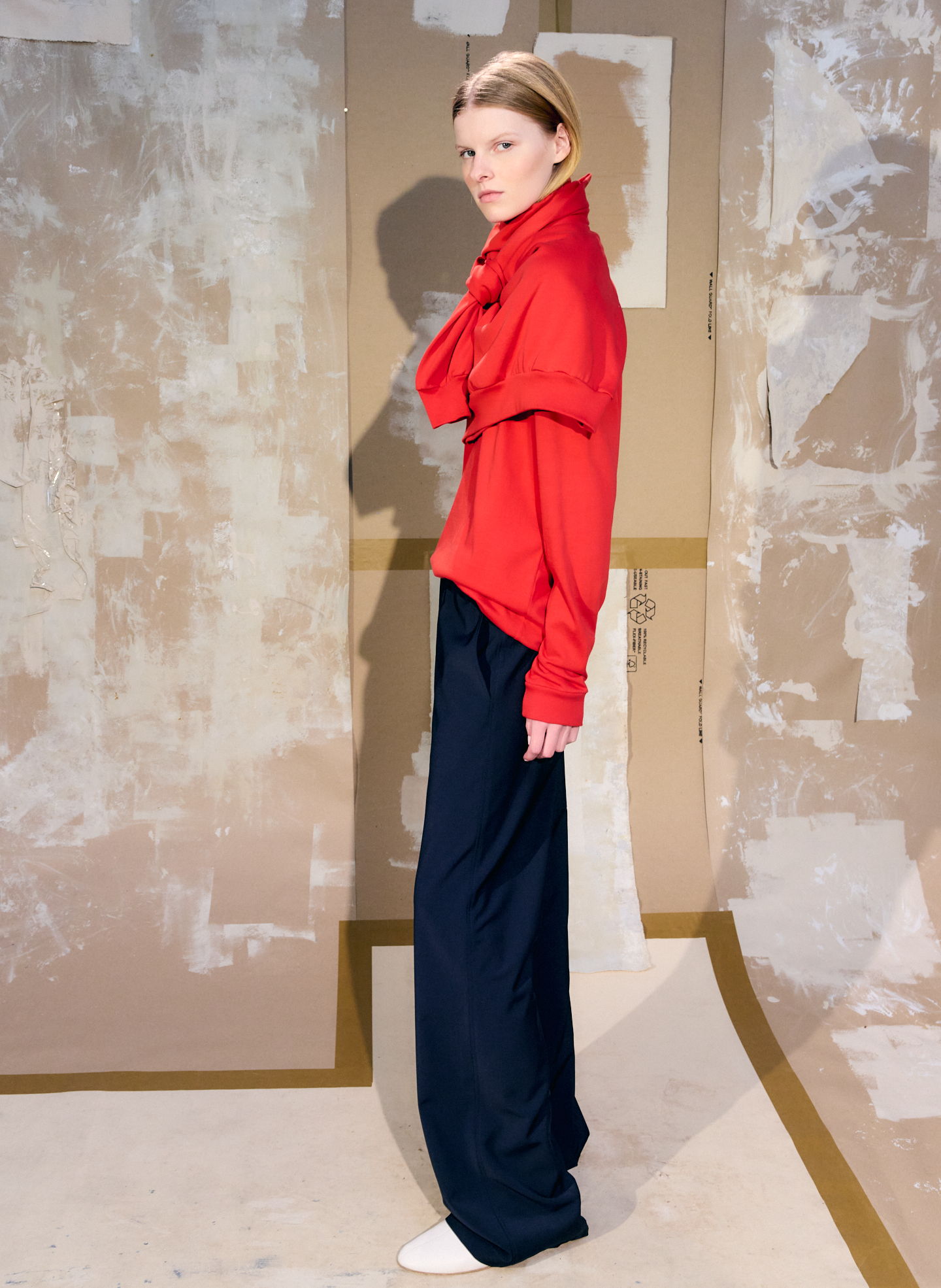 Model wearing a red top and navy pants in a studio setting.