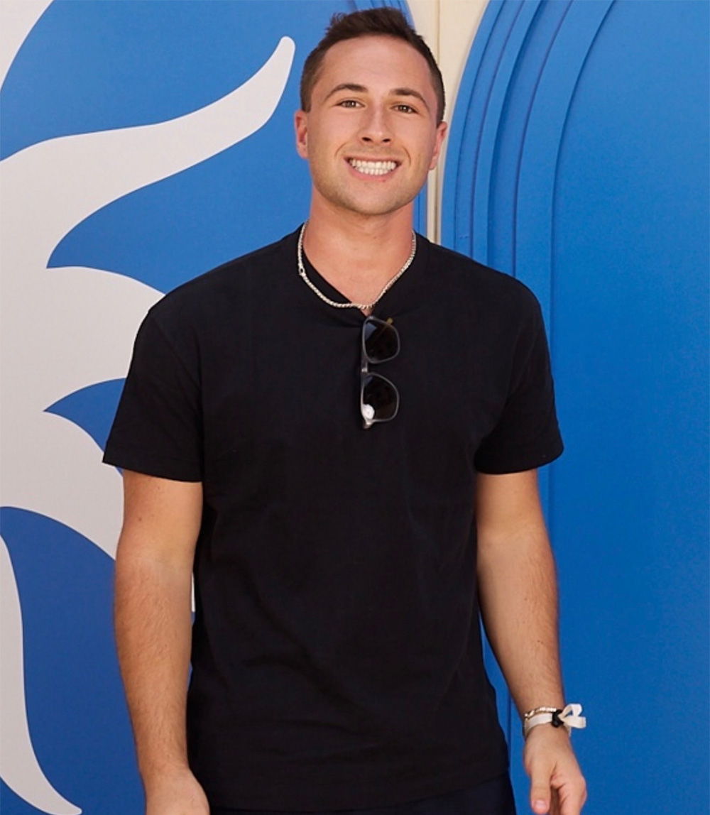 Smiling person in a black shirt standing in front of blue background.
