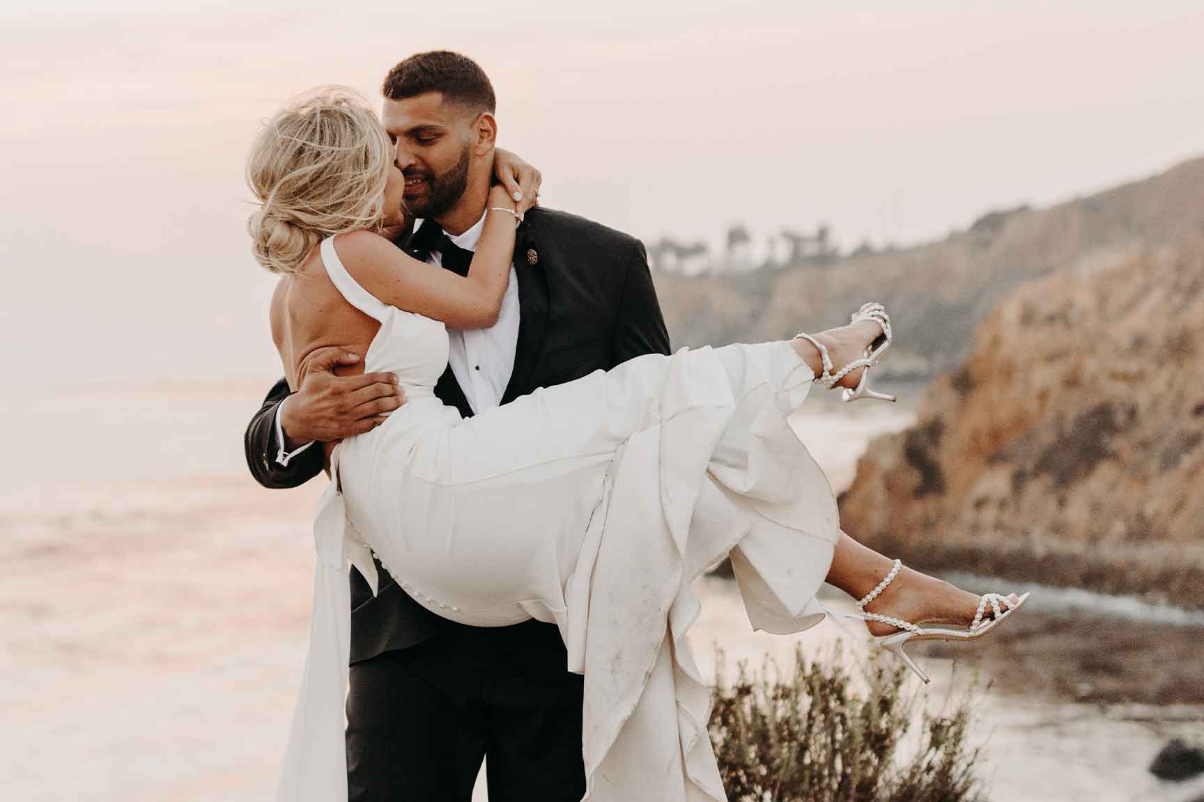 Groom holding bride with ocean coastline in background