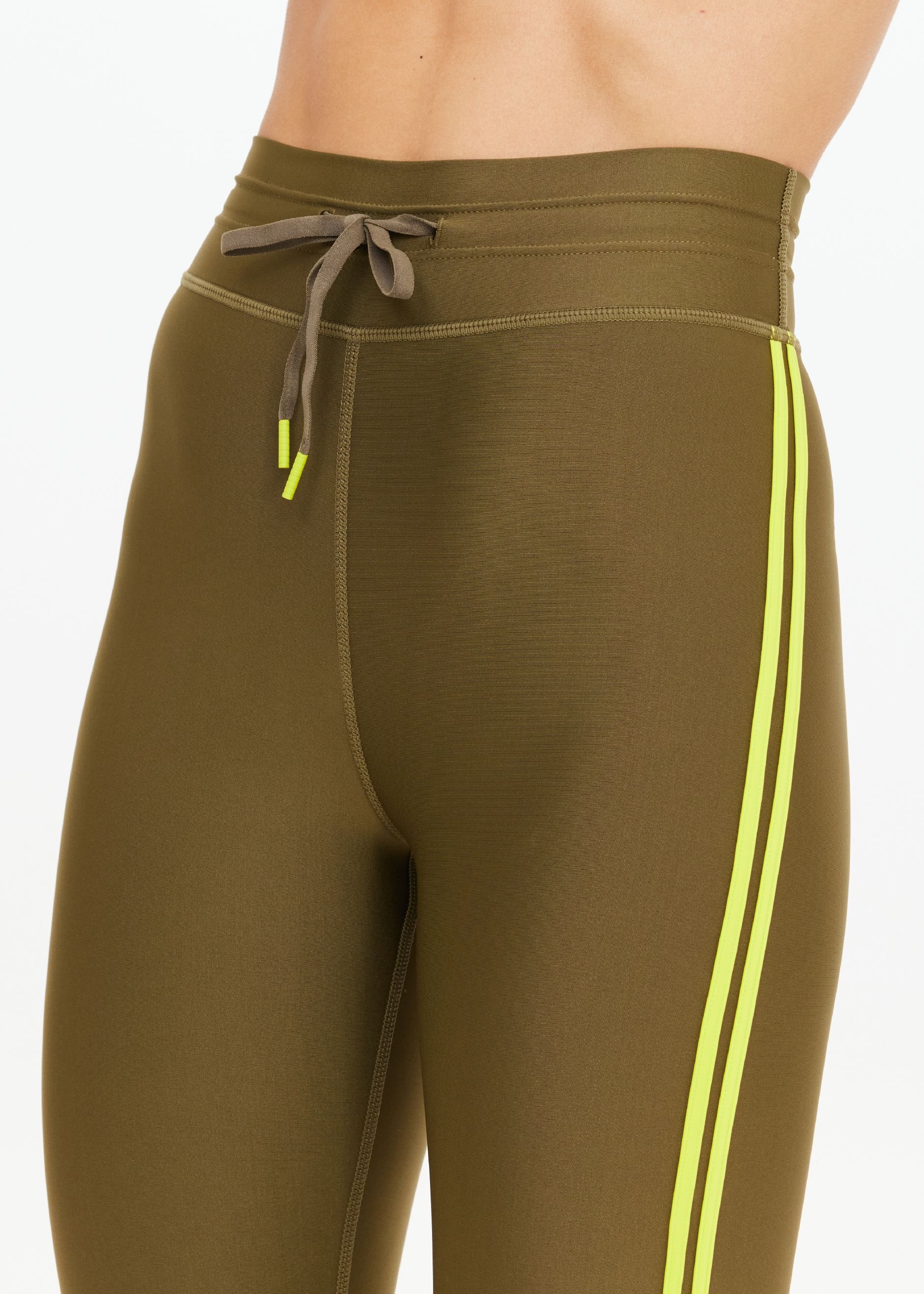 Woman wearing olive green leggings with yellow side stripes and white sneakers.
