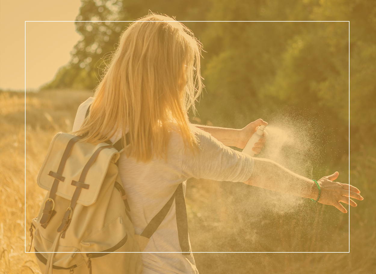 Une jeune femme en randonnée estivale vaporisant de l’insectifuge sur son bras pour éviter les piqûres et les symptômes d’allergie