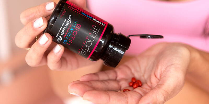 Opened Biotin vitamin B7 in hand, pouring vitamins into other hand.