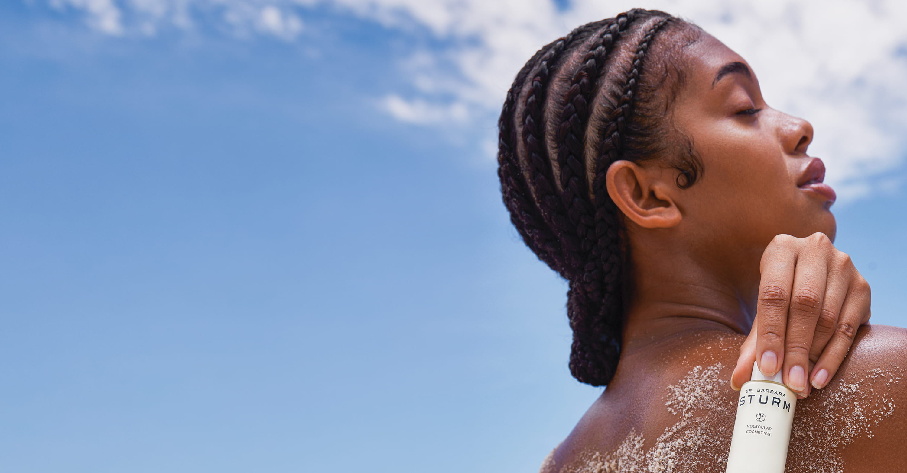 Person applying lotion on their back against a clear blue sky.