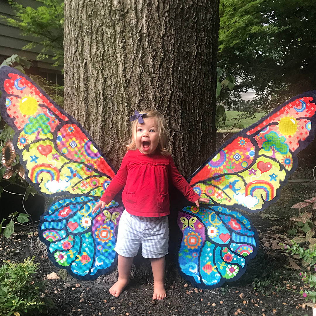 Toddler girl with large butterfly wings crafted from Perler fuse beads