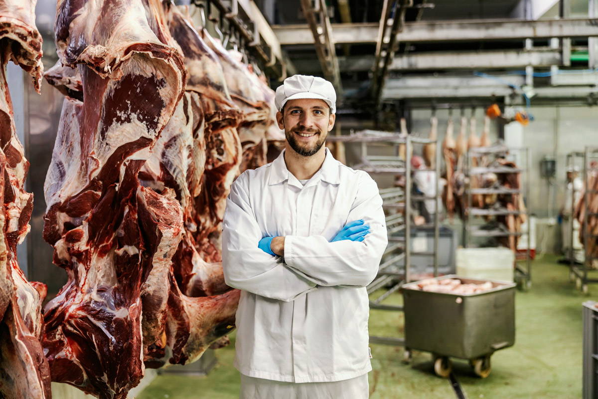 A man smiling in a meat plant, meat hanging around the room