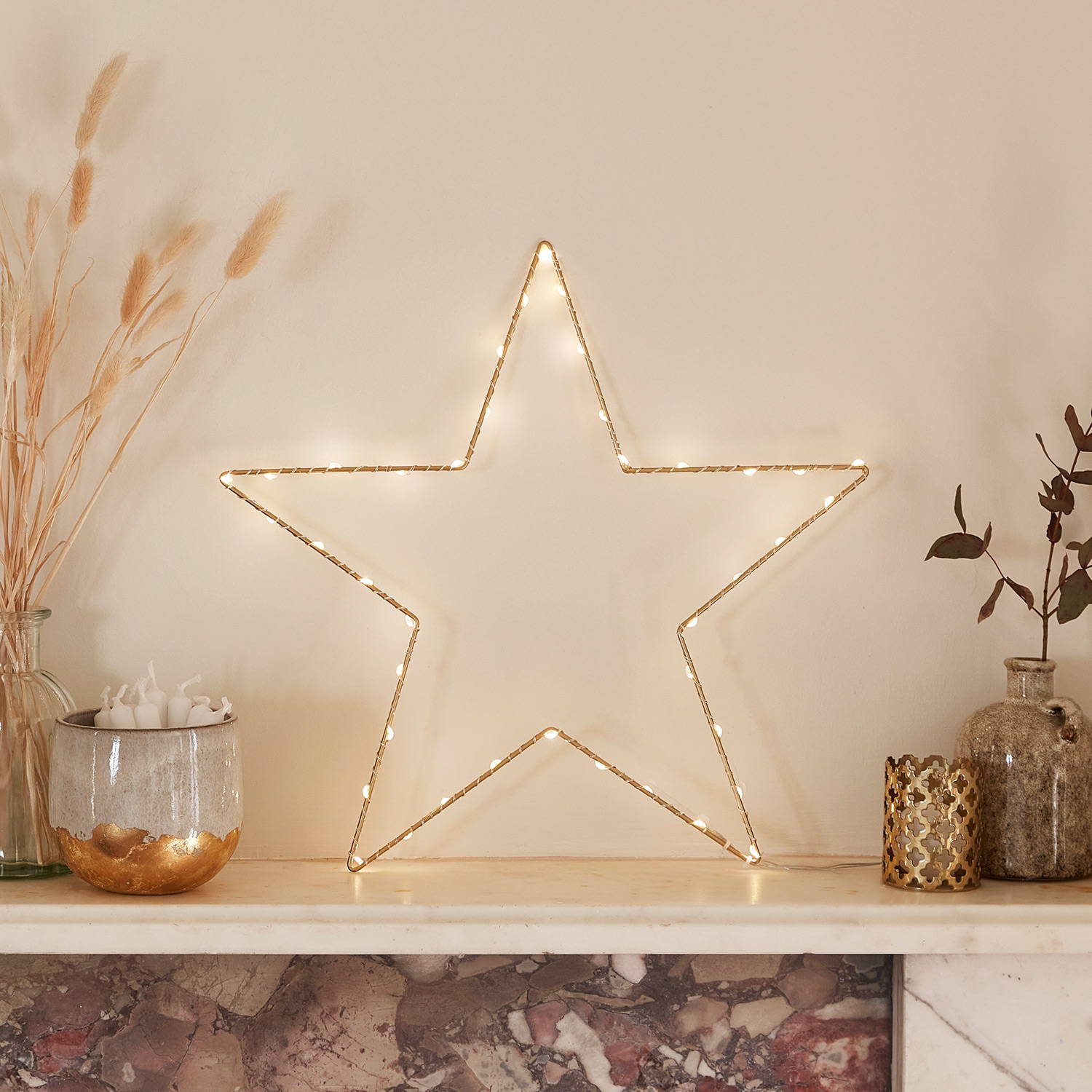 Gold Osby star on a mantlepiece with other ornaments and dried flowers.
