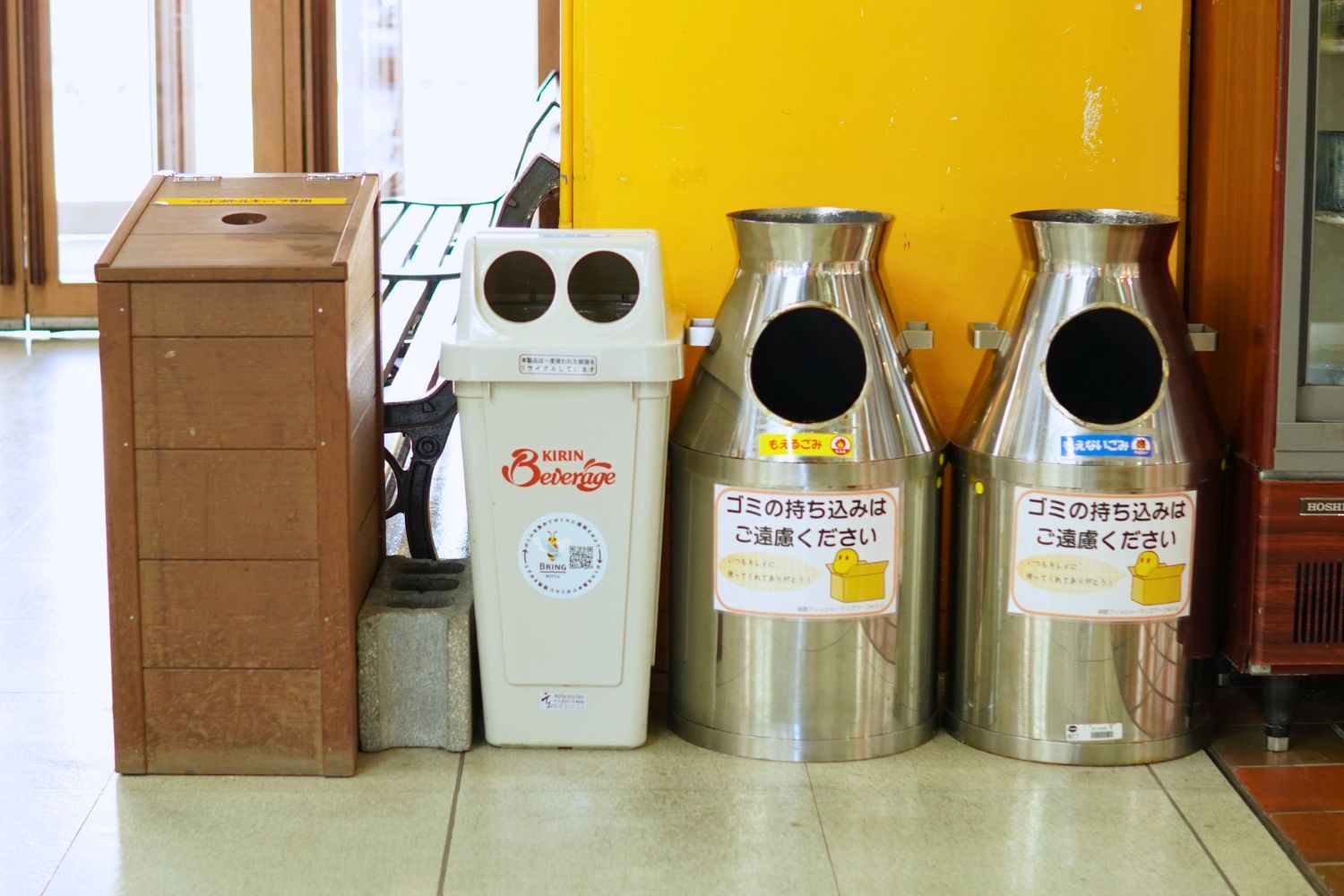 Three recycling bins and a trash can in a bright space.