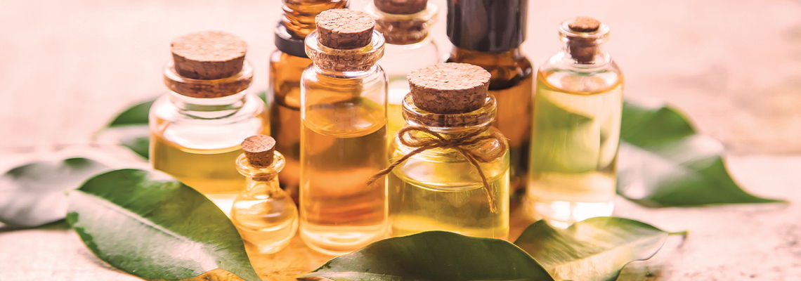 Bottles of essential oils surrounded by green leaves on a wooden surface.