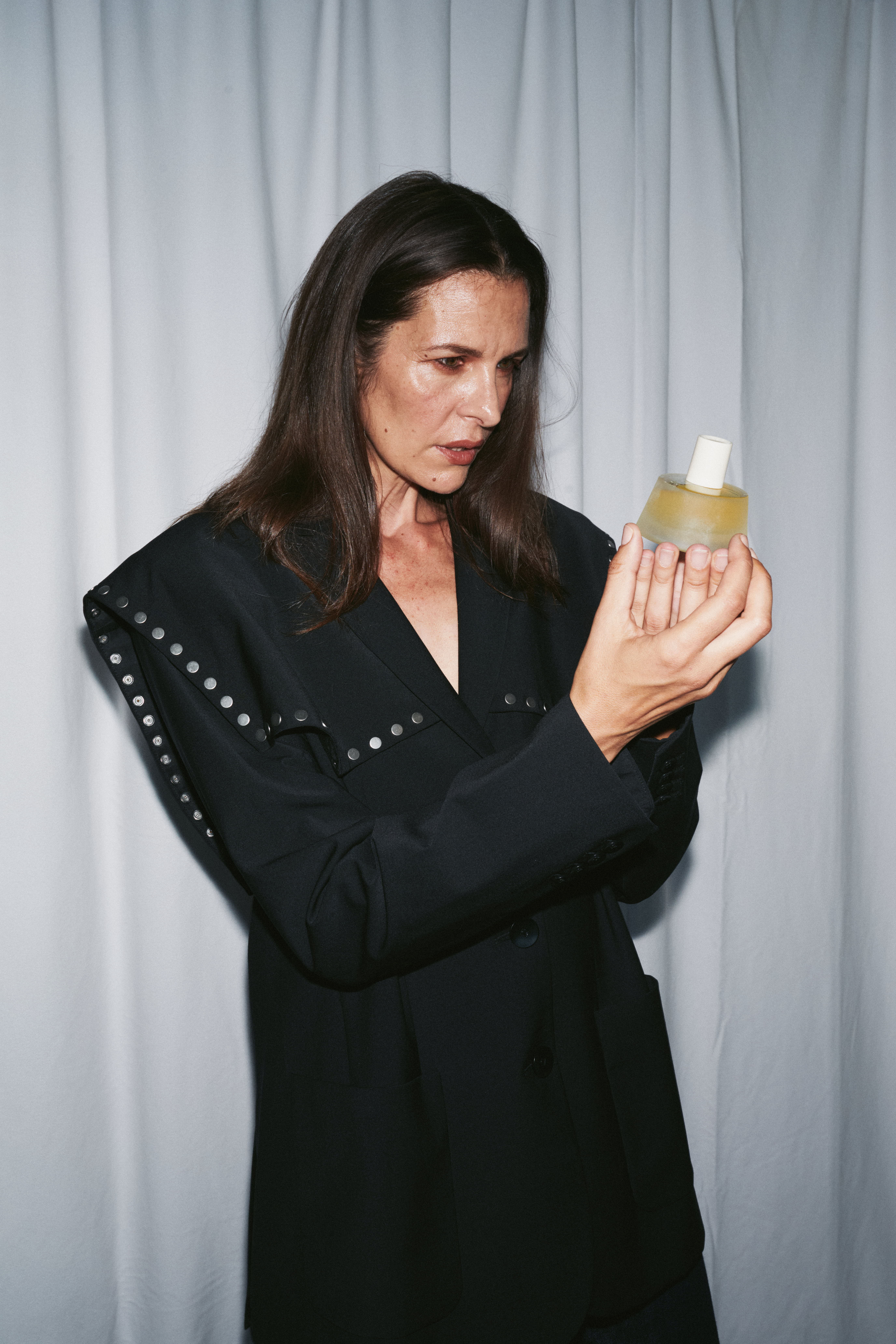 Woman in black outfit holding a bottle, looking thoughtfully at it.