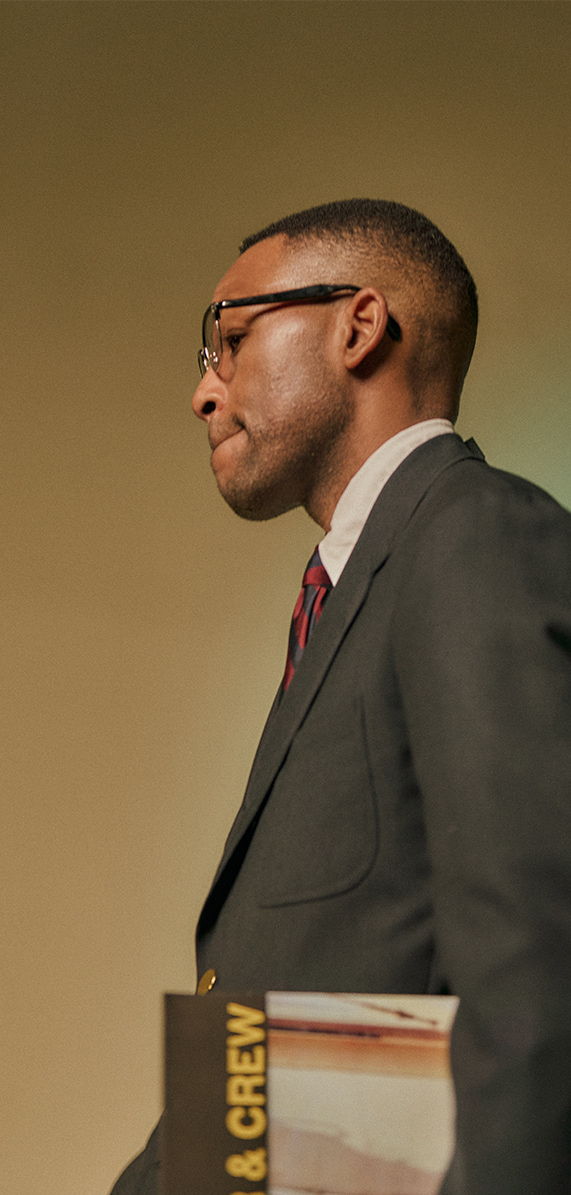 A man in a suit walking, holding a booklet.