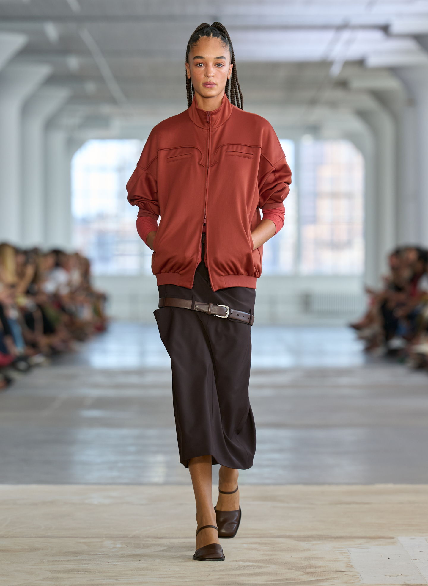 Model walking down runway in a red jacket and black skirt.