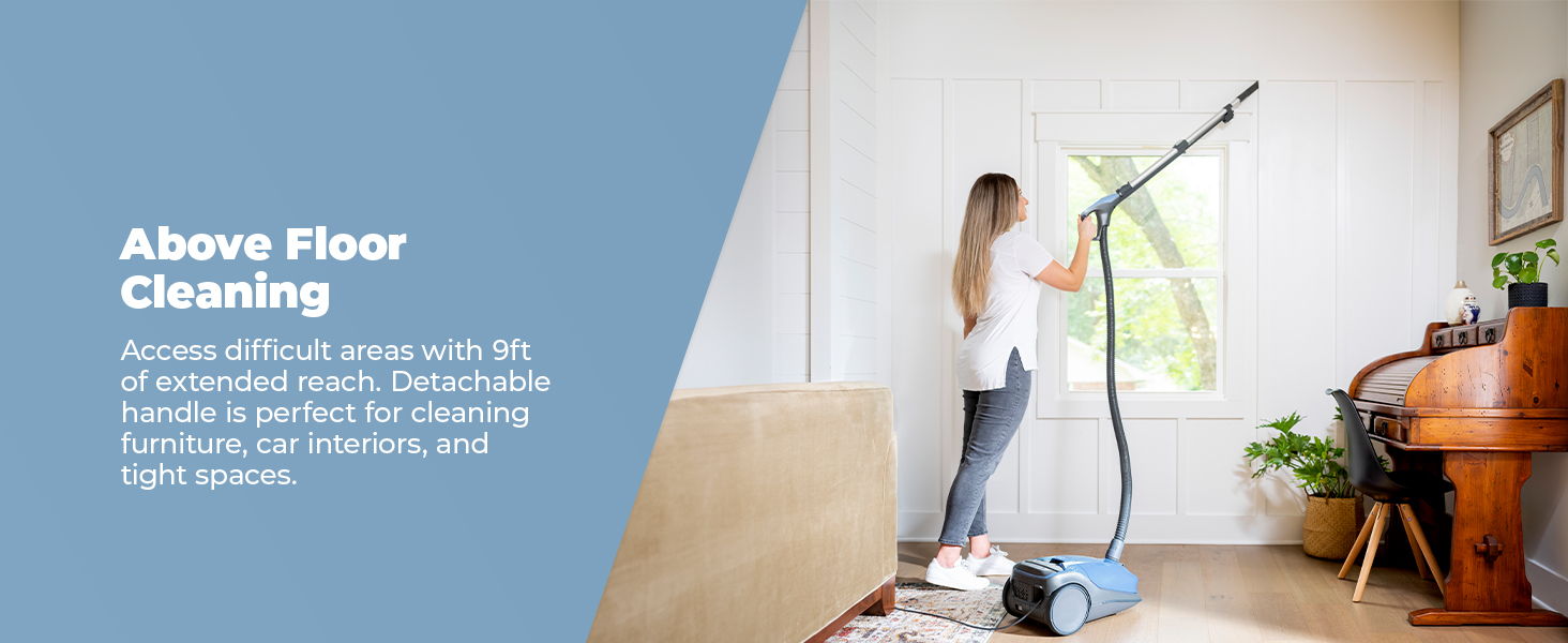 Woman using a cleaning device near a window in a bright room.