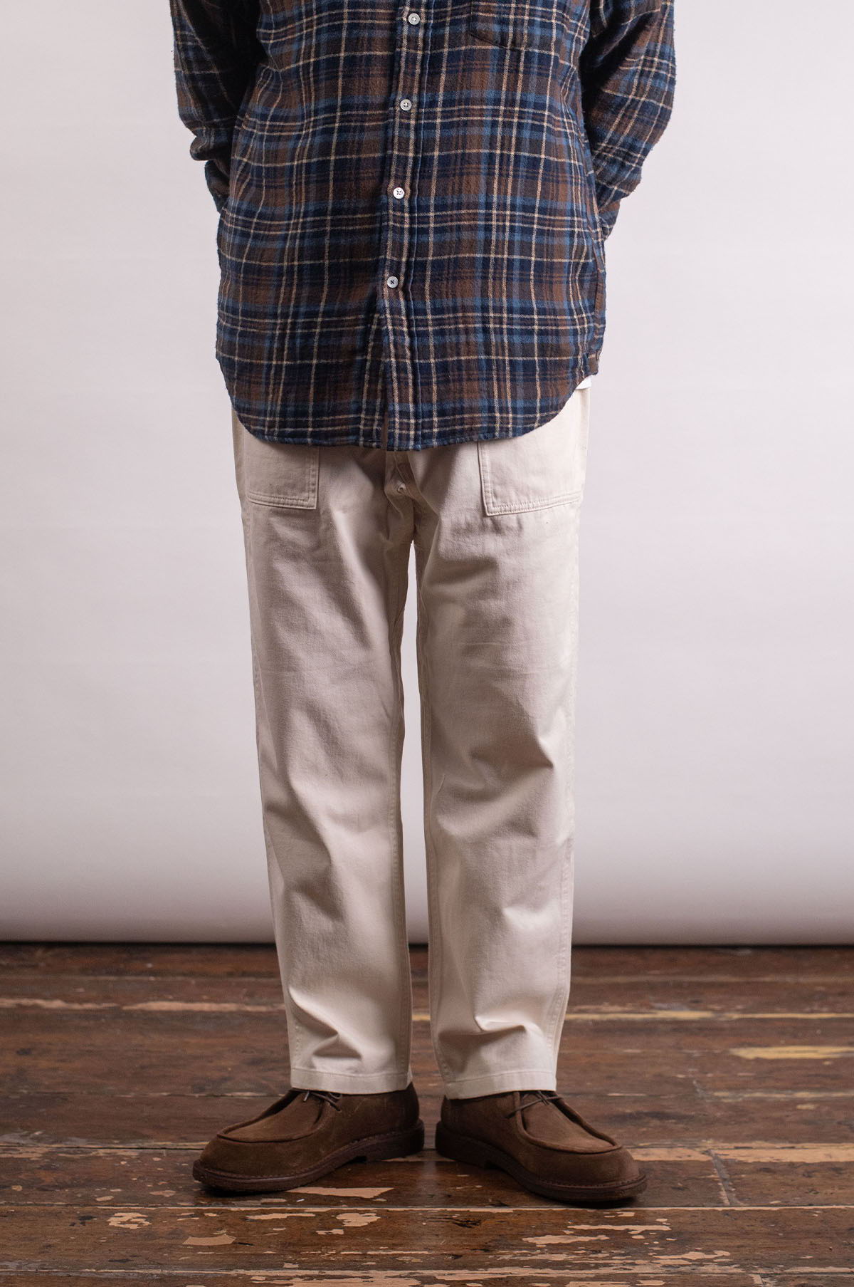 Person wearing a plaid shirt and light-colored pants standing on wooden floor.