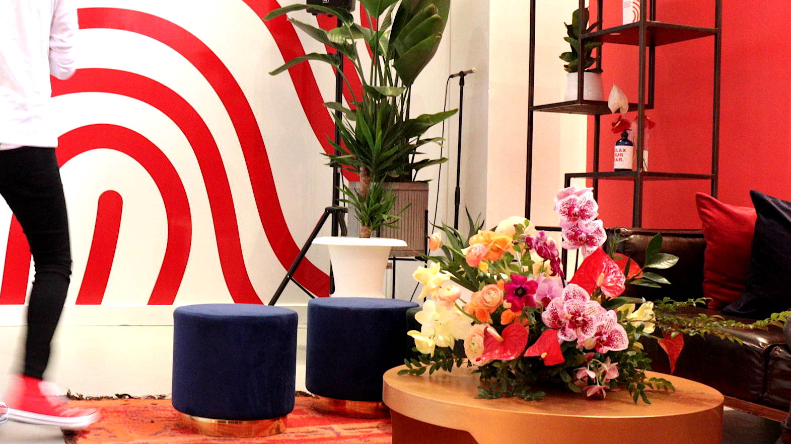 Floral arrangement on coffee table in room with couch, chairs, plants and a persons leg