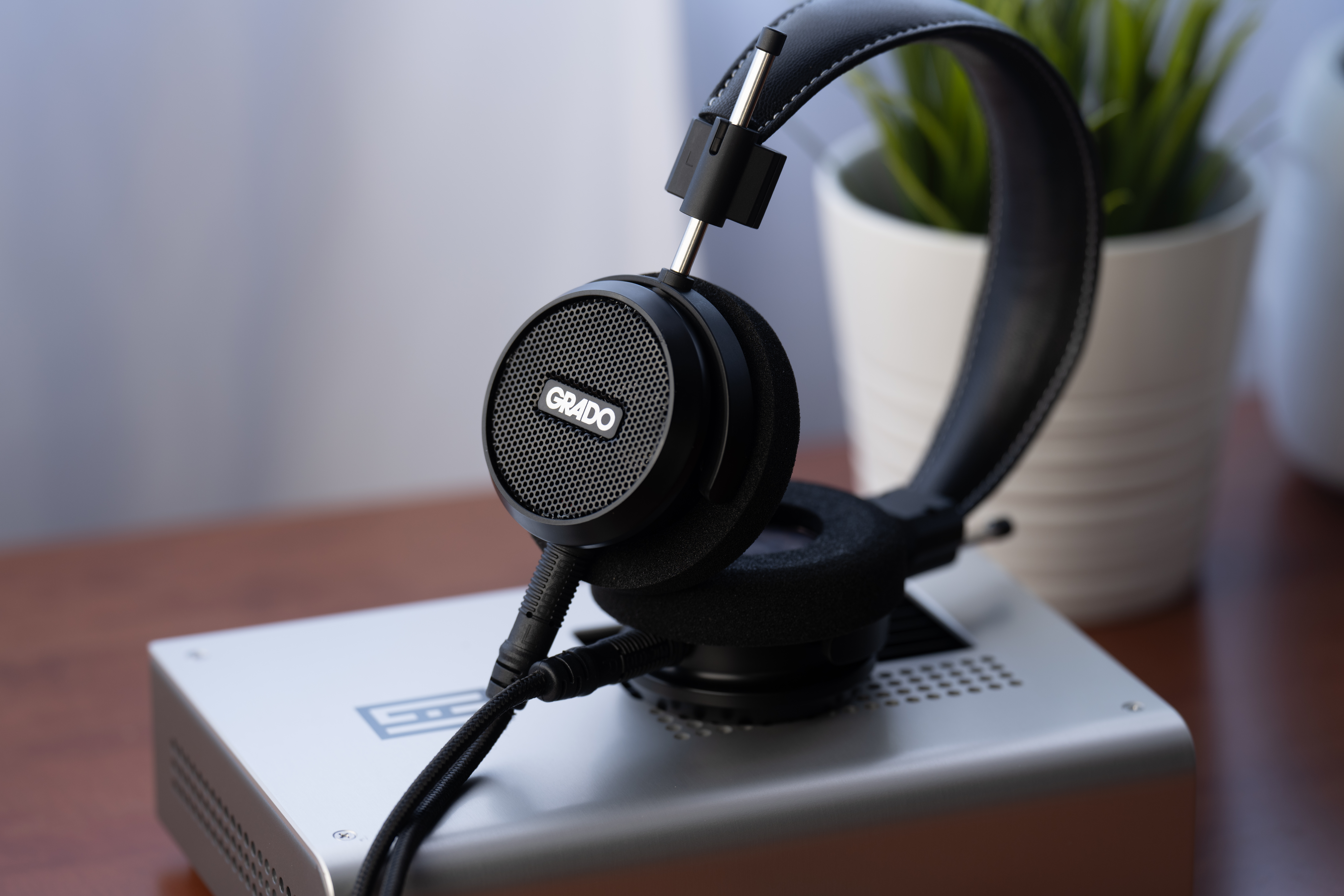Photo of the Grado S150 resting on one of it's ear cups on a silver box on a wooden table.