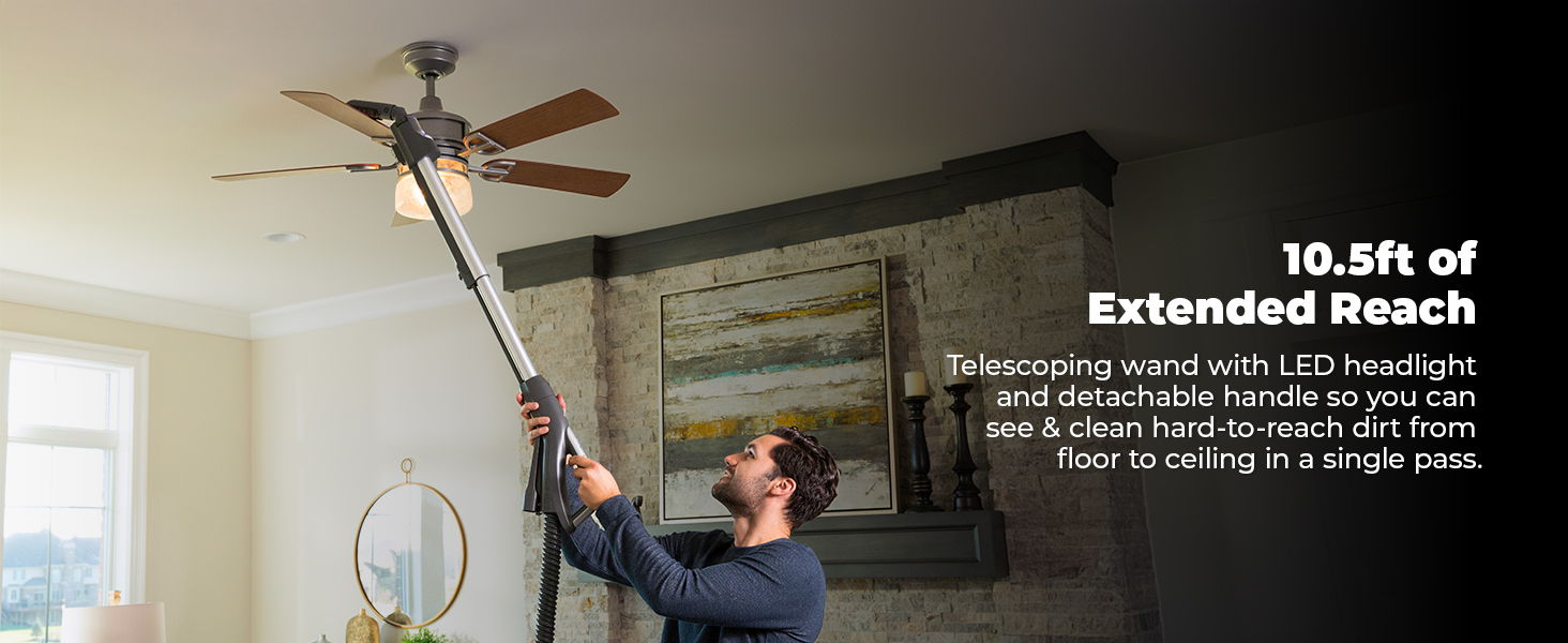 Person using a long pole to clean a ceiling fan indoors.