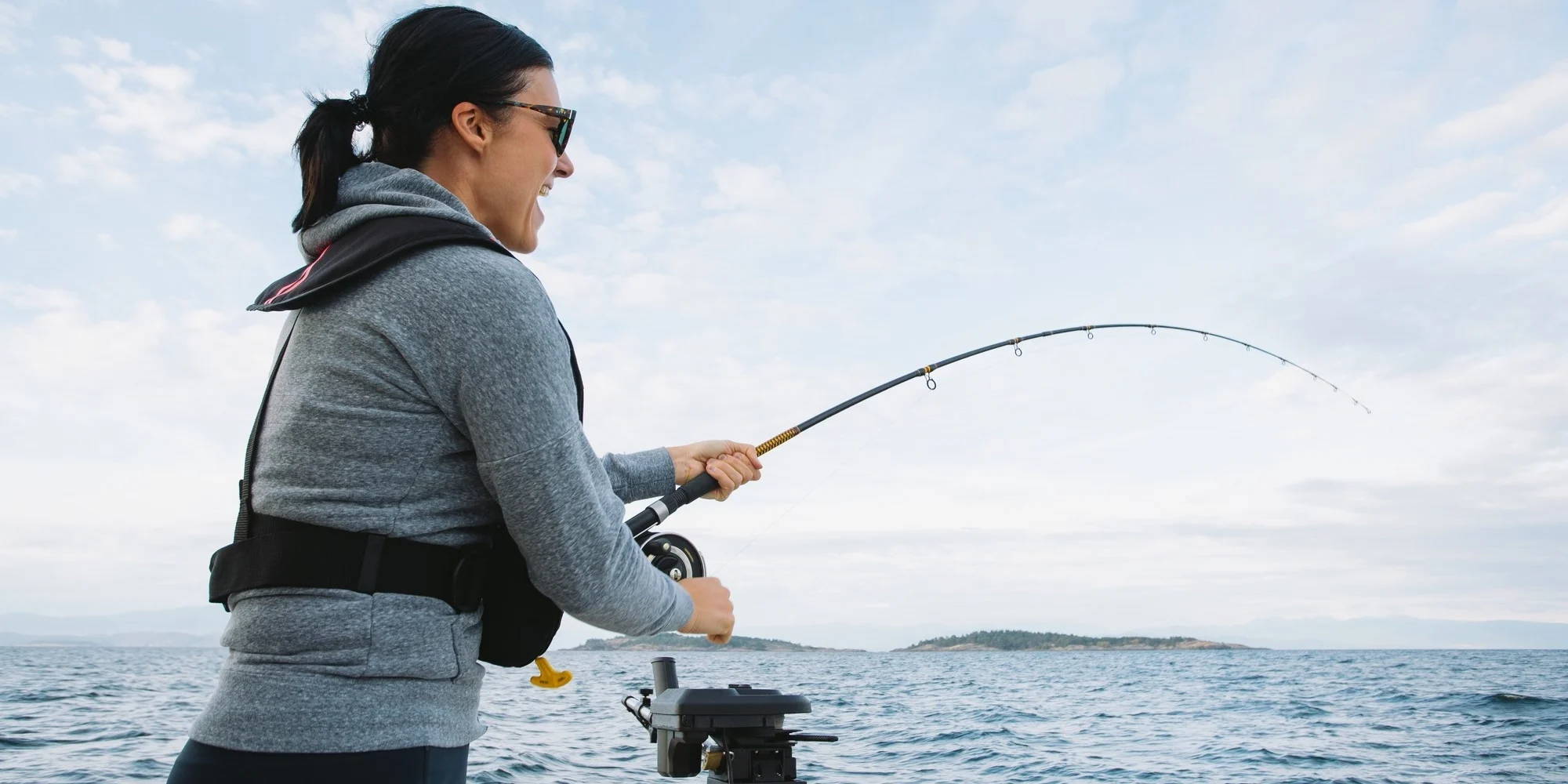 Woman wearing fishing sunglasses and holding a fishing rod. 