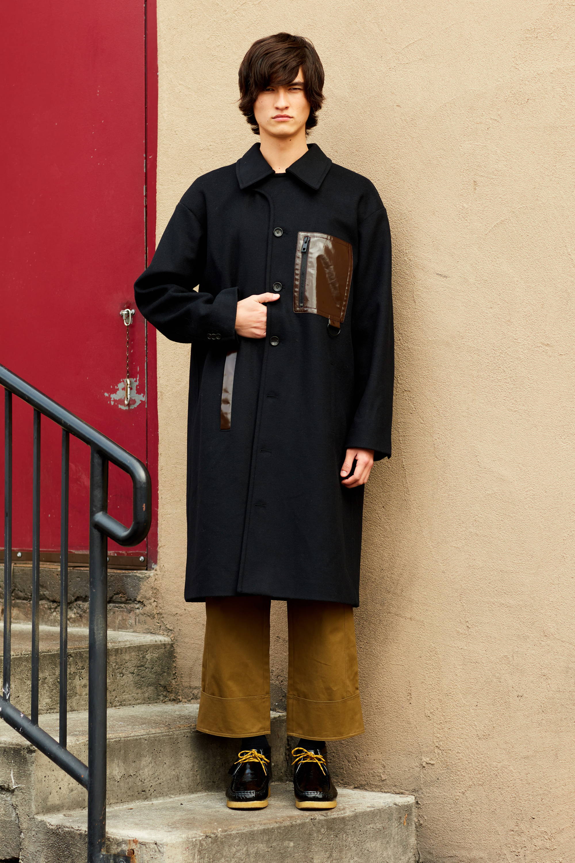Person wearing a black coat and brown pants stands on stairs.