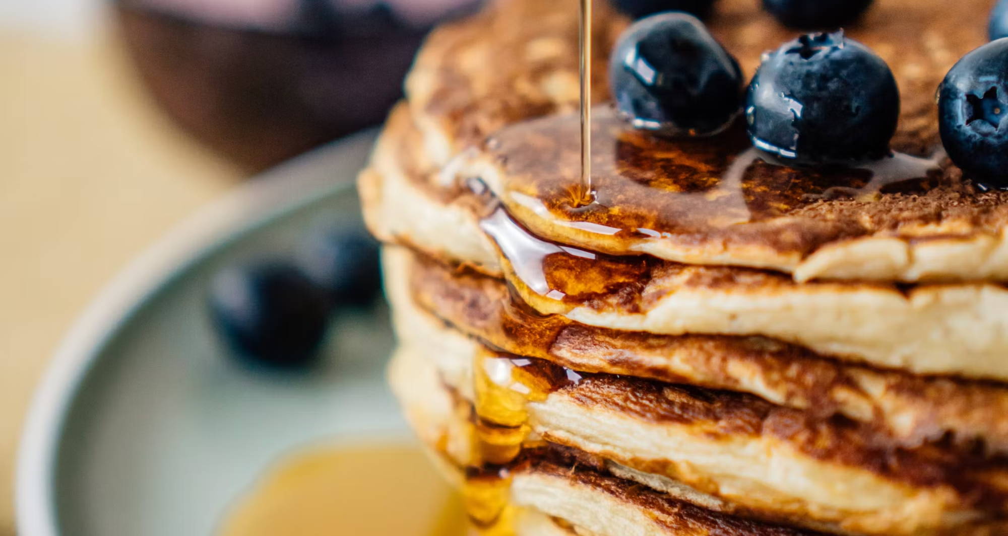 maple syrup being poured onto a stack of blueberry pancakes
