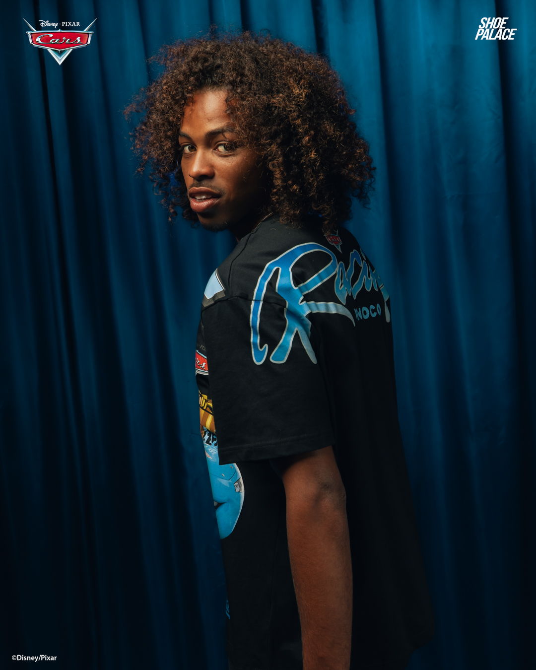 Person with curly hair wearing a graphic t-shirt against a blue backdrop.