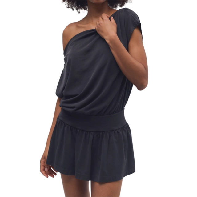 A person wearing a black off-shoulder dress, smiling, standing with one hand on hip.