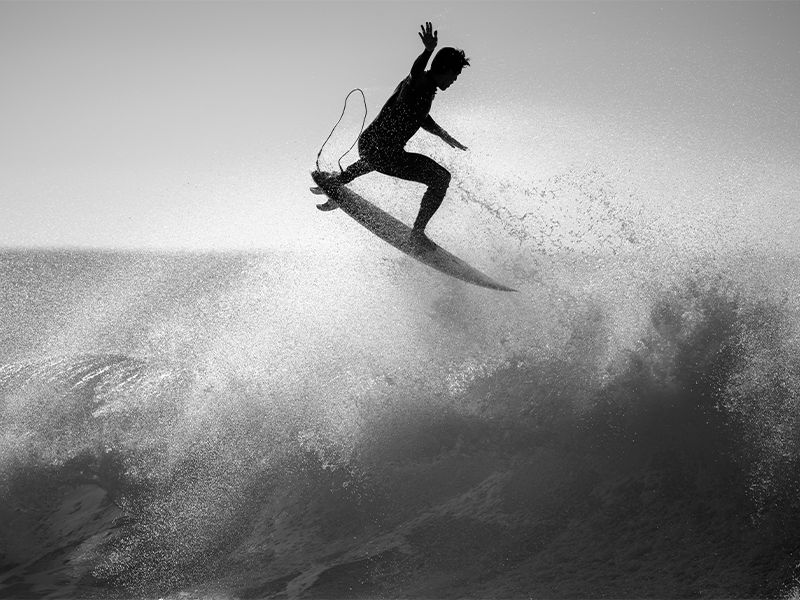 Silhouette of a surfer jumping over a wave in black and white.