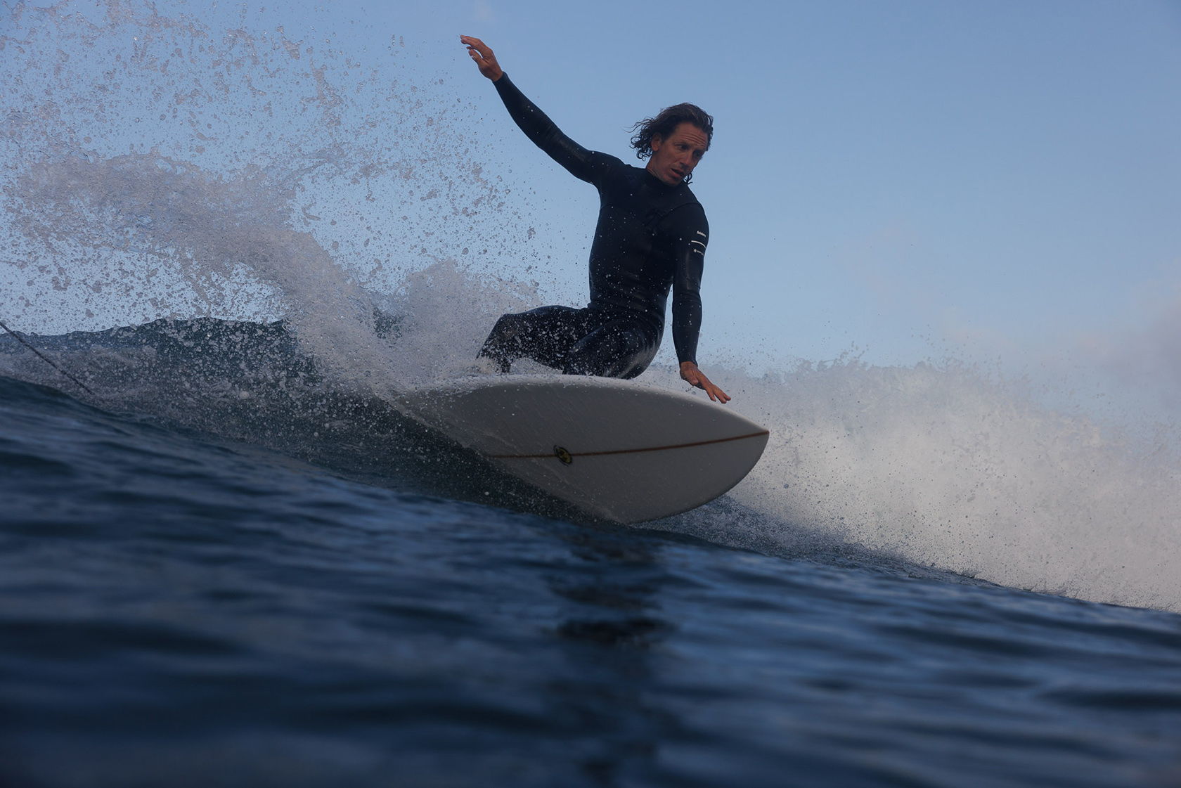 Surfer riding a wave on a surfboard against a clear sky.