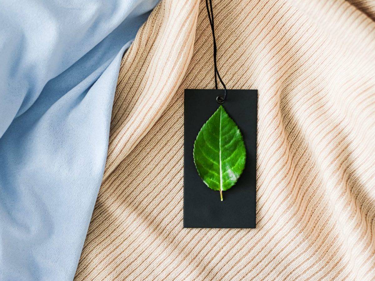 A sustainable fashion tag with a green leaf on it for a light beige shirt 