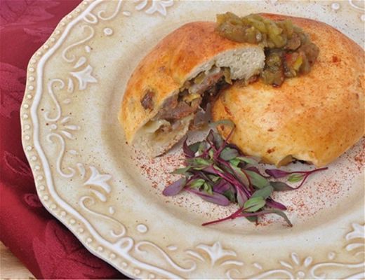 Baked pastry filled with meat and topped with sauce, garnished with microgreens.