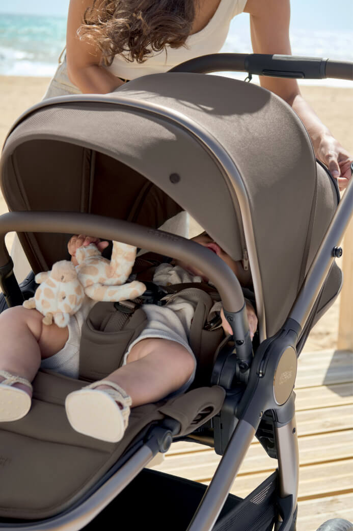 A baby in a stroller on a beach with a toy.