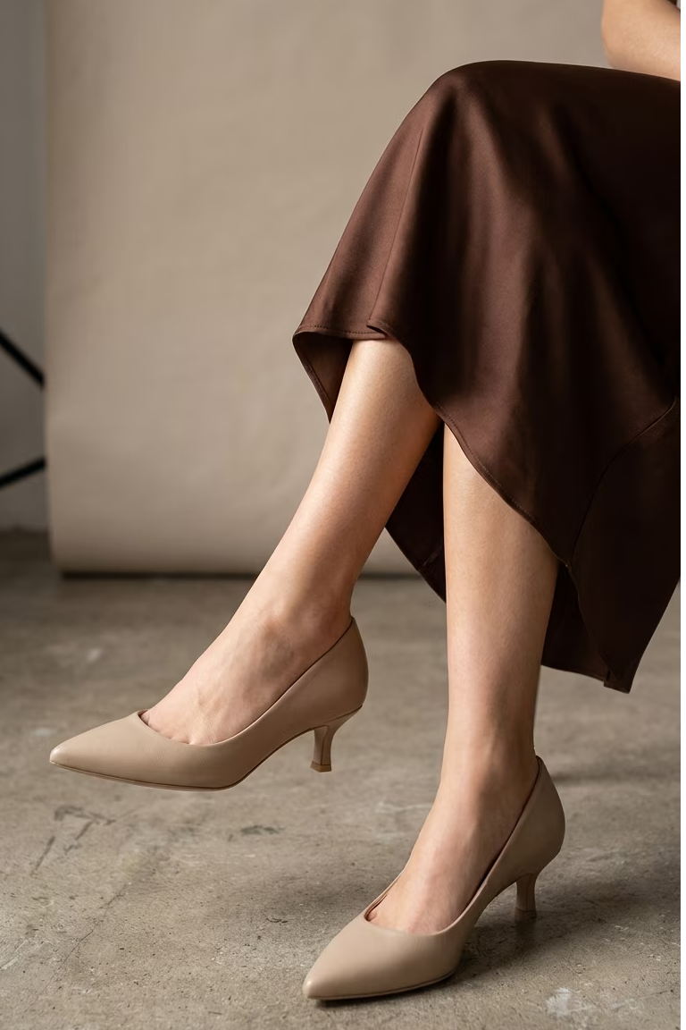 A pair of legs wearing beige high heels and a brown skirt.