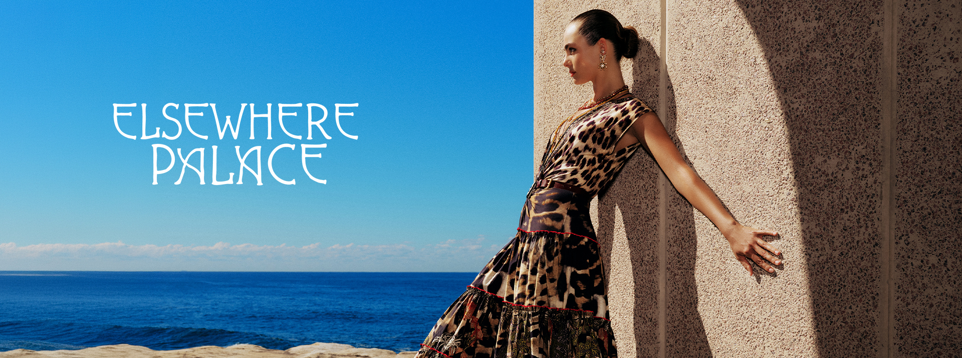 A woman in a patterned dress poses against a coastal backdrop.