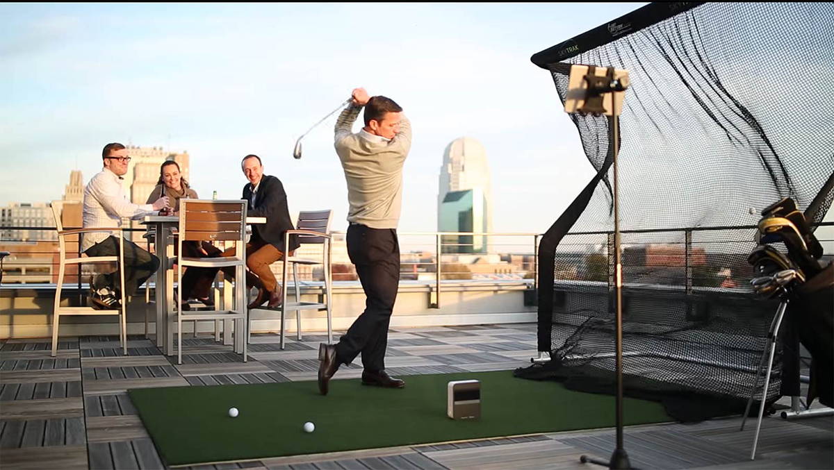 Four people using a rooftop gold simulator setup with the SkyTrak golf launch monitor