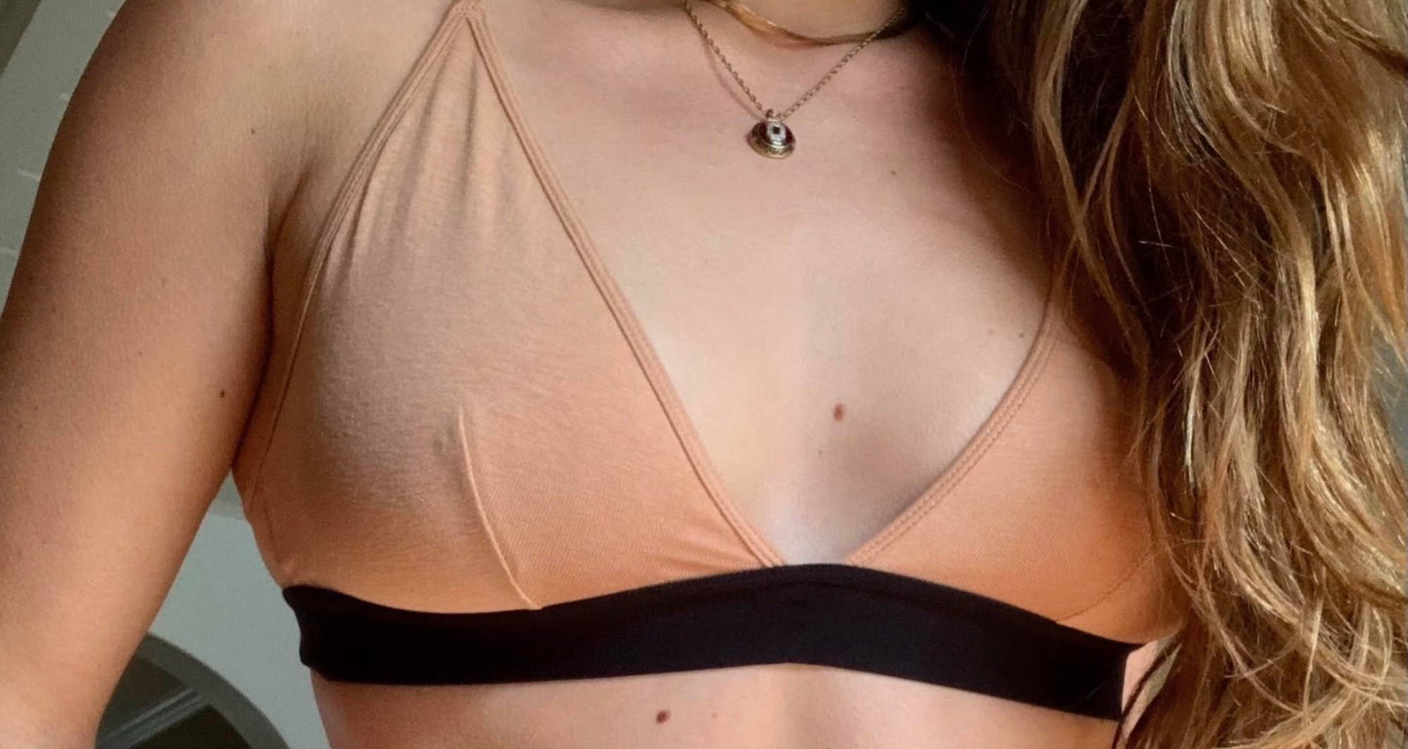 woman’s chest wearing a nude color triangle bralette with her hair over one shoulder wearing a gold necklace