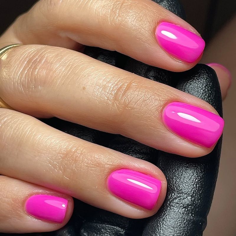 A hand with bright pink nail polish on fingers.