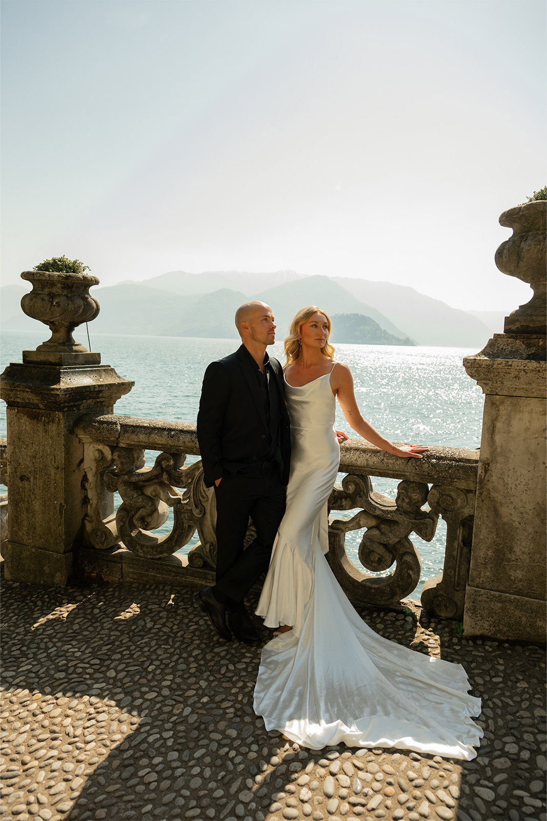 Couple in wedding attire posing by a scenic waterfront.