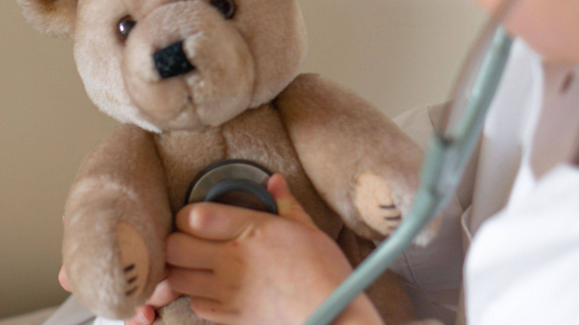 Kind in een witte jas speelt doktertje – met een stethoscoop wordt de knuffelbeer onderzocht