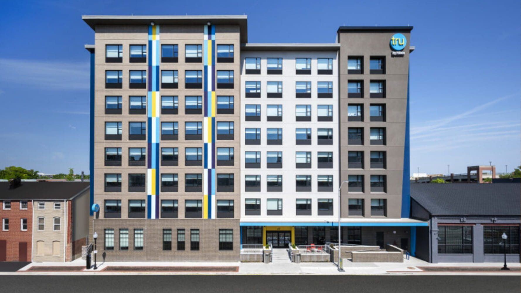 Front of the Tru by Hilton hotel in downtown Baltimore on a sunny day, with its blue and yellow striped facade, a budget friendly stay near Power Plant Live!