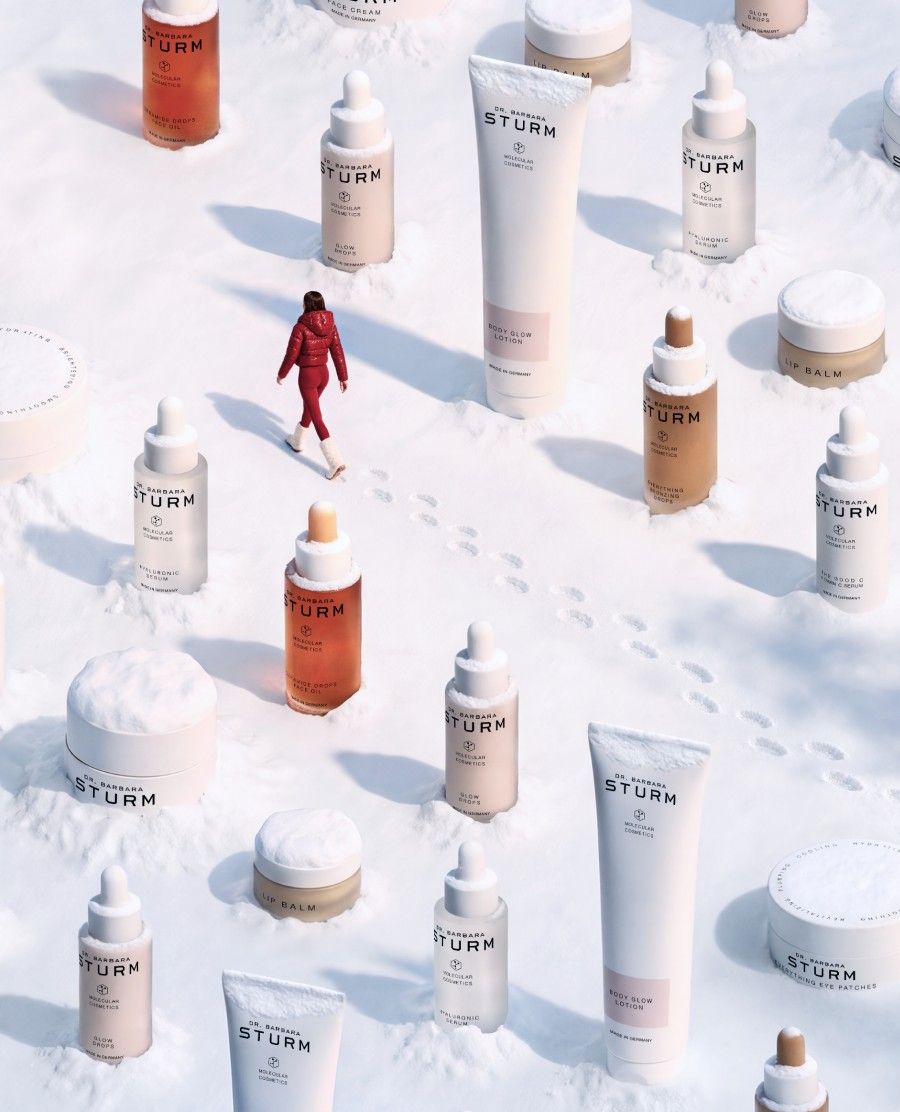 A person in red walks among various skincare products on a snowy surface.
